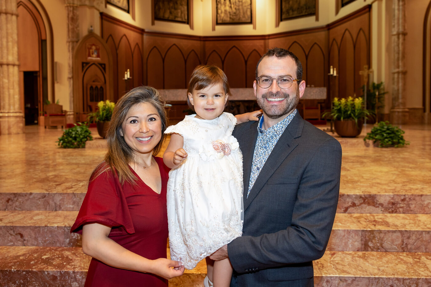 women in red dress holding infant with man in suit at holy name cathedral baptism professional photographer