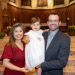 women in red dress holding infant with man in suit at holy name cathedral baptism professional photographer