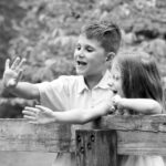 Portrait of young boy and sister with hands up over a bridge