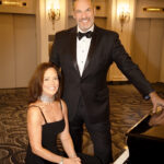 man in black tuxedo posing playing with woman in black gown seated at piano at Hilton hotel chicago