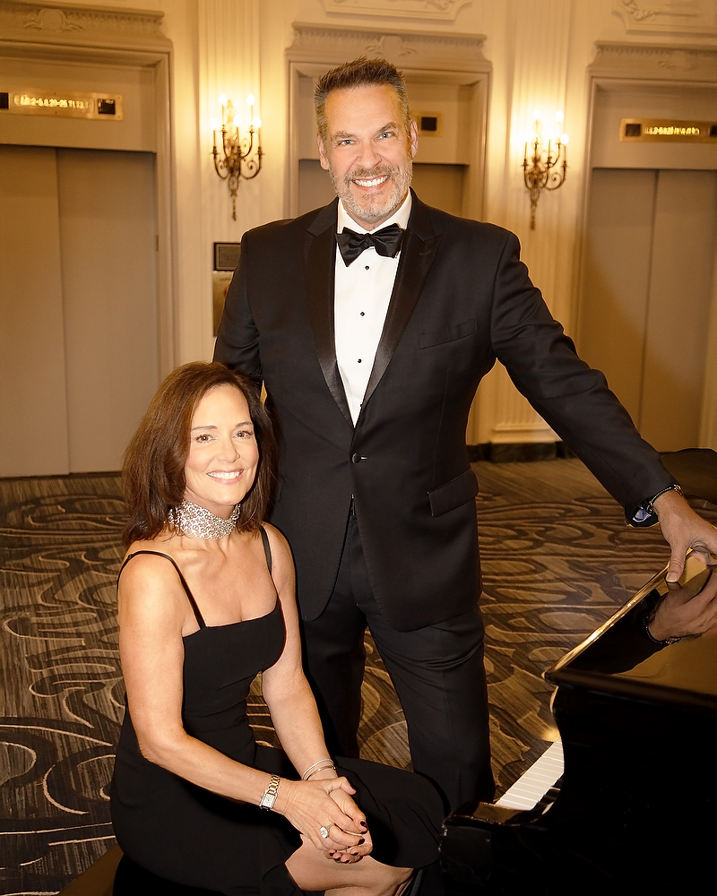 man in black tuxedo posing playing with woman in black gown seated at piano at Hilton hotel chicago