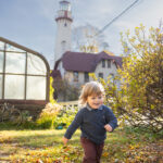 boy running in sunlight at lighthouse beach wearing red pants and navy sweater