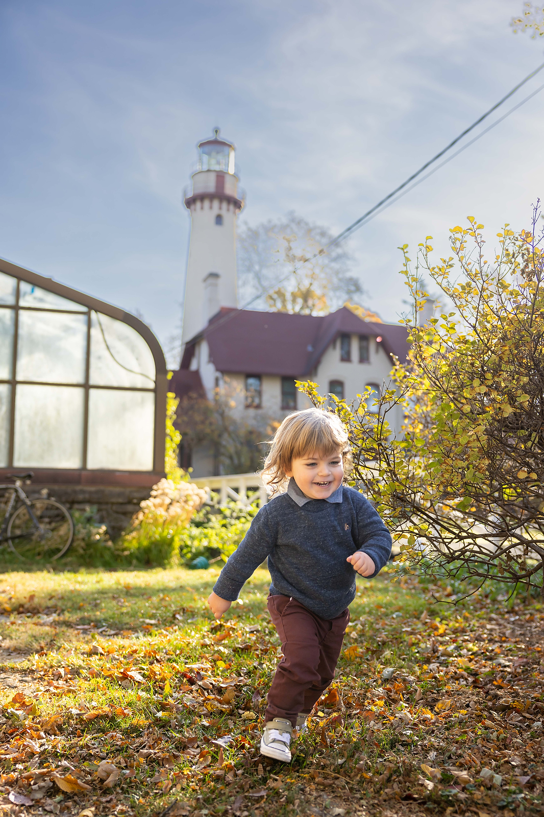 boy running in sunlight at lighthouse beach wearing red pants and navy sweater